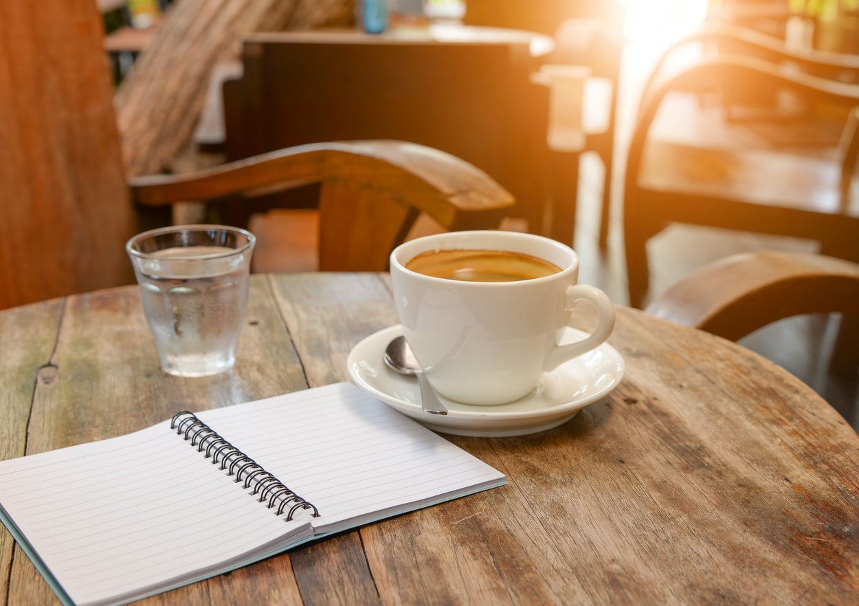 Coffee with notebook and water glass on wooden table.